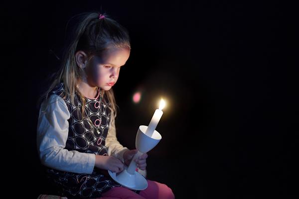 Kaitlyn holds a candle in front of her, lighting her face